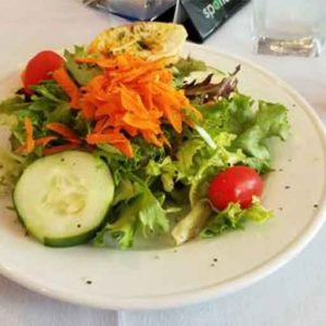 A plate of salad on a table next to a glass of water.